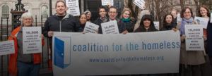 Advocates from the Coalition for the Homeless and Legal Aid Society wearing winter coats and holding signs that read "16,000 homeless families need action" and a banner with the Coalition for the Homeless logo.