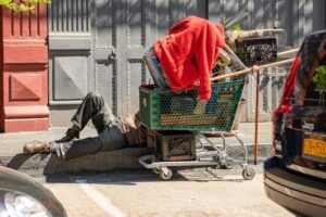 a homeless man asleep under a shopping cart