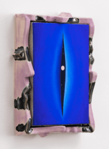 A small, rectangular painting features a central image of a narrow, vertical slit that gradually transitions from deep blue at the edges to a lighter blue at the center. Inside the slit, a black sky is visible, dotted with small white stars and a single pink sphere, resembling a planet. The painting is mounted in a sculptural frame that appears to be made of a glossy, ceramic material in shades of soft pink and black. The piece is displayed against a plain white wall.